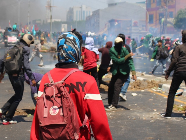 Bilden visar flera maskerade personer på en gatan där något typ av upplopp sker