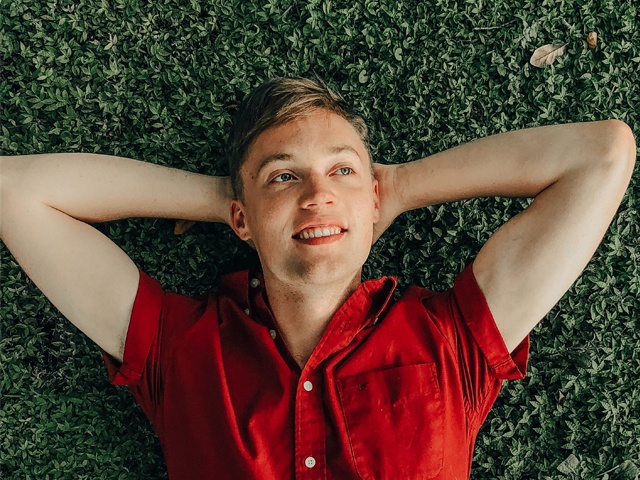 Bilden visar en kille som ligger på gräs och tittar snett uppåt med ett leende som om han känner sig nöjd