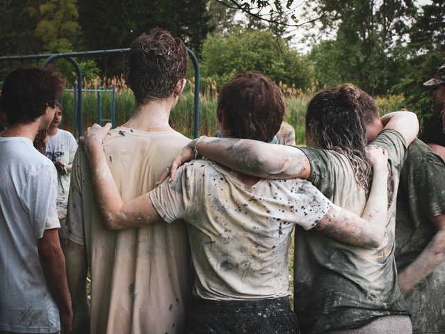 Bilden visar en grupp med unga som står med ryggen mot och håller om varandra