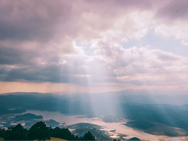 Bilden visar ett landskap där solen lyser vackert genom molnen mot jorden