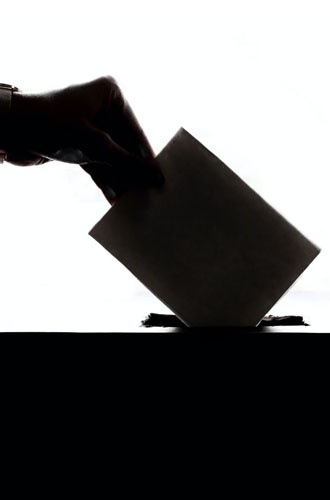Bilden visar en hand som lägger sitt valkuvert i en röstlåda